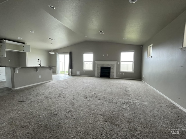 unfurnished living room with vaulted ceiling, baseboards, plenty of natural light, a tile fireplace, and a textured ceiling