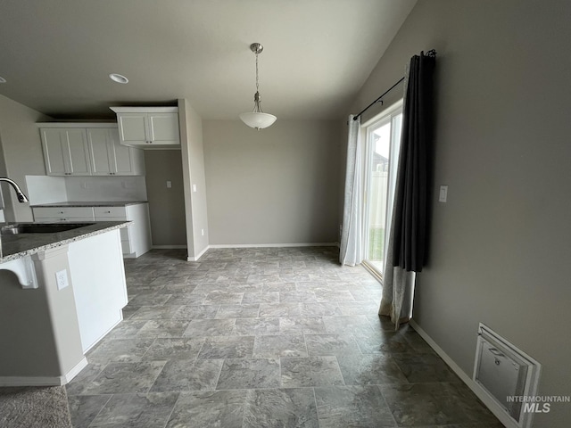 kitchen with a sink, light stone finish floors, white cabinetry, baseboards, and pendant lighting