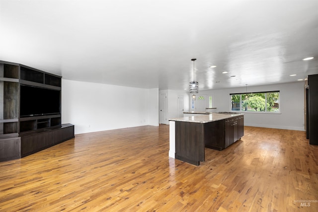 kitchen featuring a center island, light wood finished floors, dark brown cabinets, baseboards, and open floor plan
