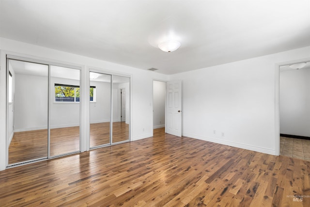 unfurnished bedroom with two closets, wood finished floors, and baseboards