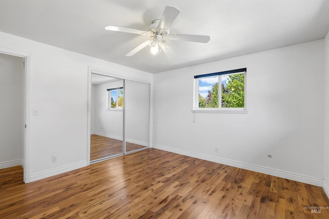 unfurnished bedroom featuring multiple windows, wood finished floors, baseboards, and a closet