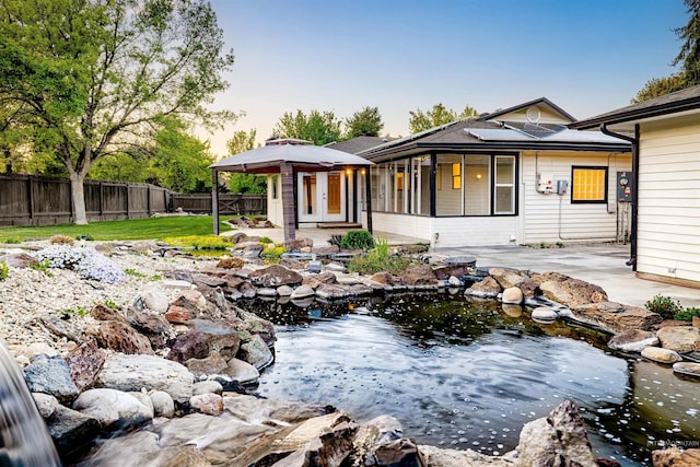 rear view of house with a fenced backyard, a garden pond, a patio, a gazebo, and roof mounted solar panels