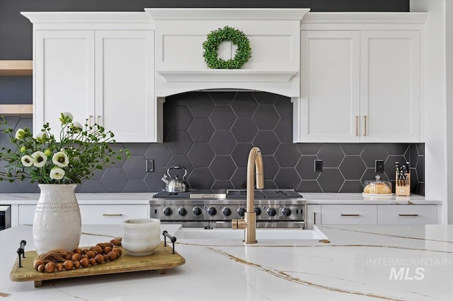 kitchen with tasteful backsplash, light stone counters, stove, and white cabinets