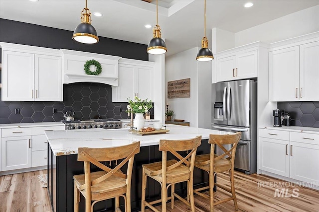 kitchen with stainless steel appliances, a kitchen island with sink, light wood finished floors, and white cabinets