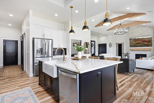 kitchen with a sink, light wood-type flooring, appliances with stainless steel finishes, white cabinetry, and light stone counters