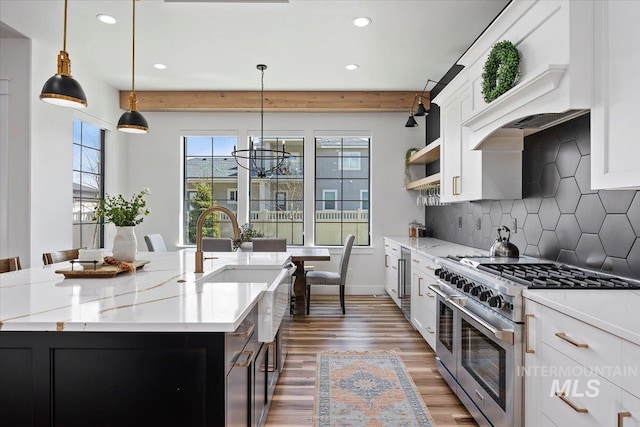 kitchen featuring high end stove, tasteful backsplash, custom exhaust hood, wood finished floors, and a kitchen island with sink
