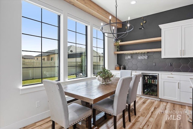 dining room with a notable chandelier, light wood-type flooring, baseboards, indoor bar, and wine cooler