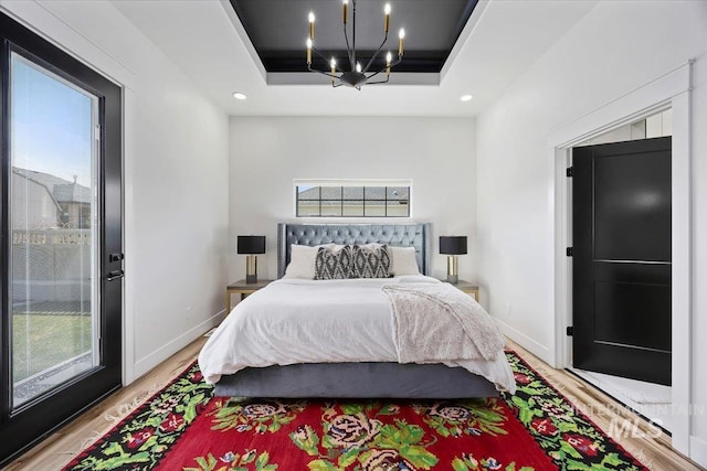 bedroom with a notable chandelier, a tray ceiling, baseboards, and light wood-style flooring