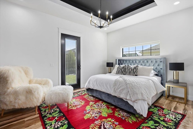 bedroom featuring a chandelier, a tray ceiling, recessed lighting, wood finished floors, and access to outside