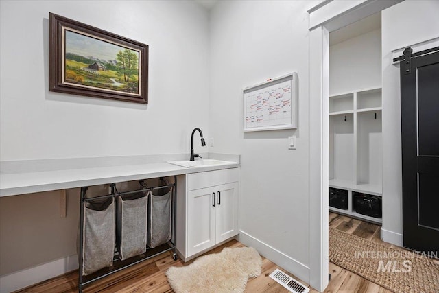 laundry room featuring baseboards, light wood finished floors, a sink, and visible vents