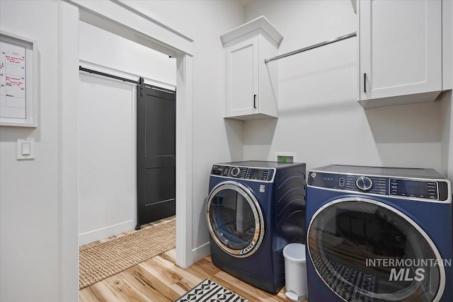 laundry area featuring cabinet space, light wood finished floors, separate washer and dryer, and a barn door