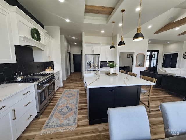 kitchen featuring appliances with stainless steel finishes, wood finished floors, a sink, a breakfast bar area, and beam ceiling