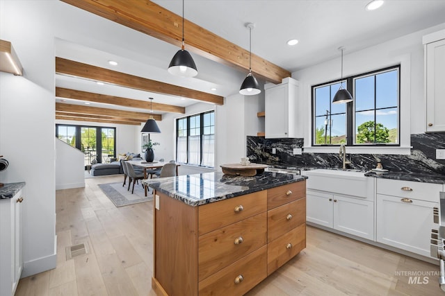 kitchen with white cabinetry, light hardwood / wood-style flooring, dark stone counters, beam ceiling, and backsplash