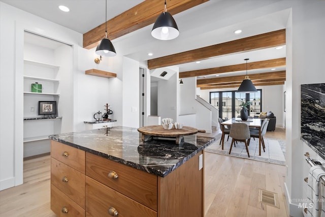 kitchen featuring beamed ceiling, hanging light fixtures, dark stone counters, and light hardwood / wood-style flooring