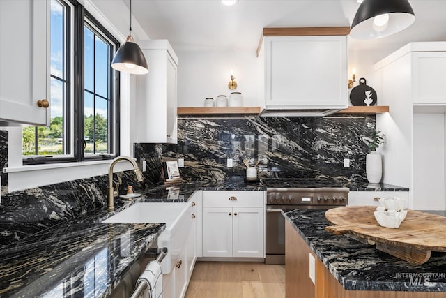 kitchen with light hardwood / wood-style floors, hanging light fixtures, stainless steel range, dark stone countertops, and white cabinets