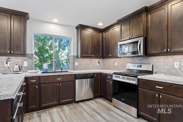 kitchen featuring dark brown cabinets, a sink, light wood-style flooring, appliances with stainless steel finishes, and backsplash