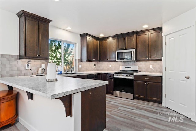 kitchen with stainless steel appliances, dark brown cabinetry, a sink, and a peninsula