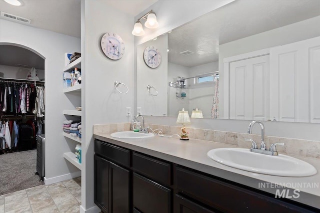 bathroom featuring visible vents, a sink, a stall shower, and double vanity