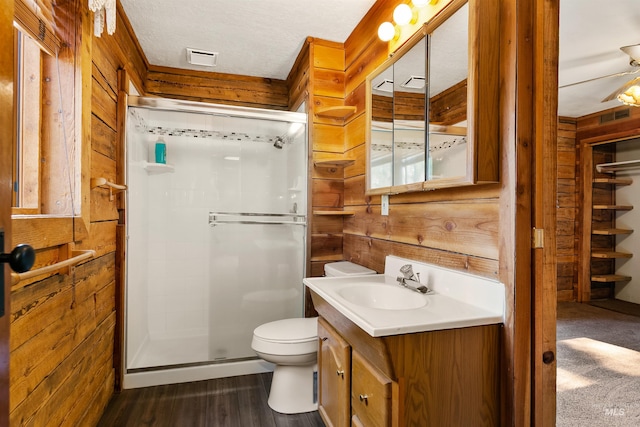 bathroom featuring vanity, wood walls, hardwood / wood-style flooring, toilet, and a shower with shower door