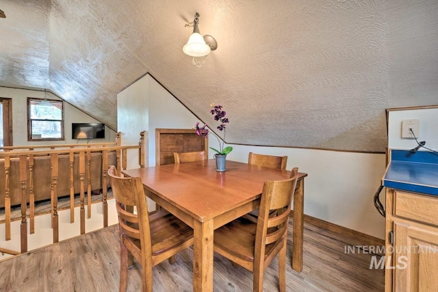 dining space with a textured ceiling, hardwood / wood-style floors, and vaulted ceiling