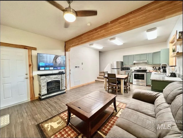 living room featuring ceiling fan, beam ceiling, light wood-type flooring, and a fireplace