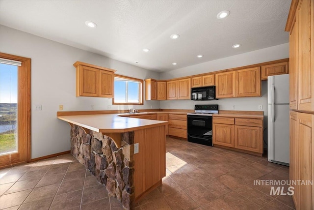 kitchen featuring electric range oven, black microwave, freestanding refrigerator, a peninsula, and recessed lighting