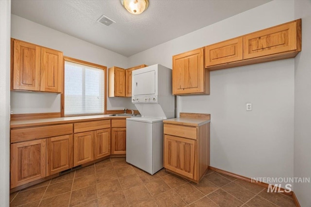 laundry area featuring stacked washer / drying machine, cabinet space, and baseboards