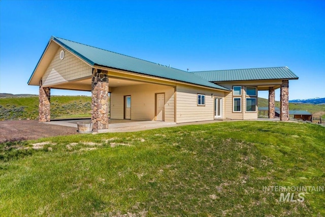 back of house with an attached carport, a patio area, a yard, and metal roof