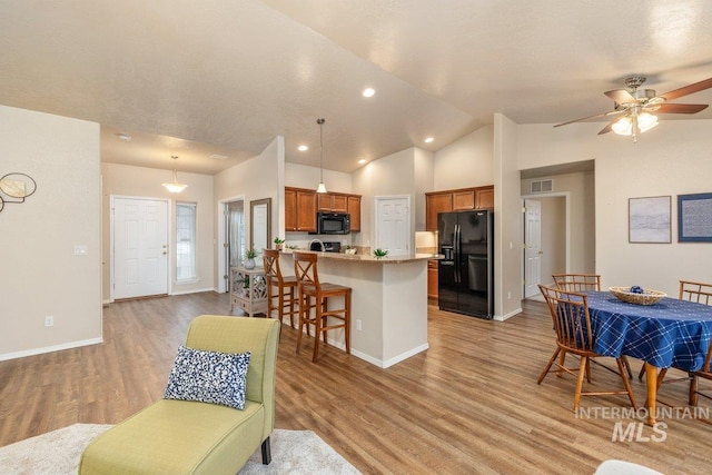 kitchen with a breakfast bar, light wood-type flooring, kitchen peninsula, pendant lighting, and black appliances