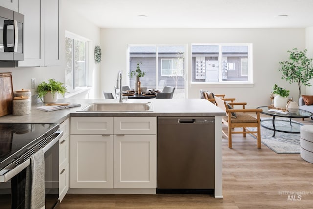 kitchen featuring stainless steel appliances, white cabinets, a sink, and light wood-style flooring