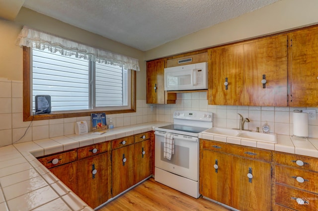 kitchen featuring a textured ceiling, white appliances, light wood-type flooring, tile countertops, and sink