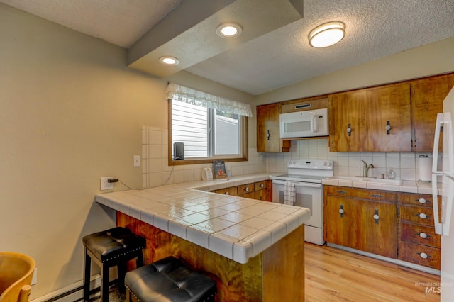 kitchen with white appliances, decorative backsplash, tile counters, light hardwood / wood-style flooring, and kitchen peninsula