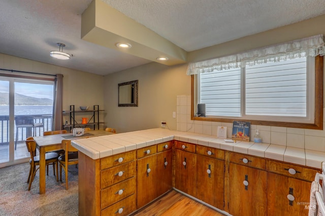 kitchen with a textured ceiling, tile counters, kitchen peninsula, and light hardwood / wood-style floors