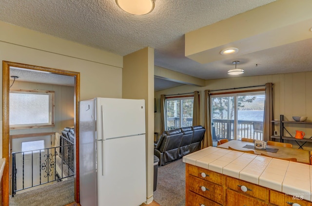 kitchen featuring tile counters, white fridge, a textured ceiling, and light carpet