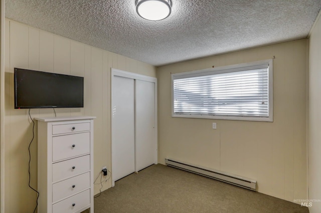 unfurnished bedroom with a baseboard heating unit, a textured ceiling, light colored carpet, and a closet