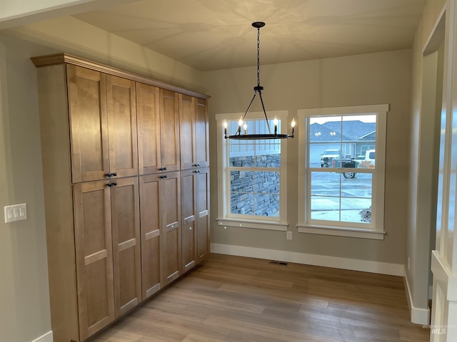 unfurnished dining area with a notable chandelier and light wood-type flooring