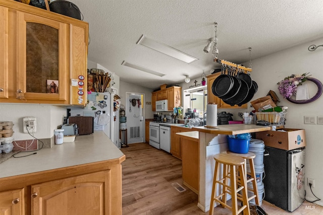 kitchen featuring white appliances, rail lighting, a kitchen bar, light hardwood / wood-style floors, and a textured ceiling