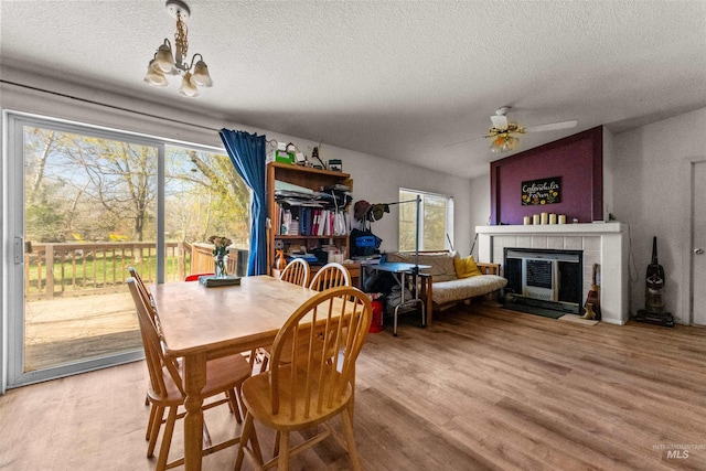 dining area with a tiled fireplace, ceiling fan with notable chandelier, a textured ceiling, lofted ceiling, and light wood-type flooring