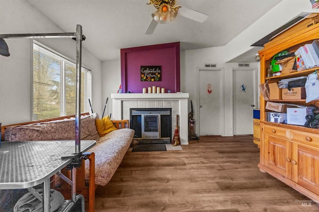 living room featuring ceiling fan, a tiled fireplace, and dark wood-type flooring