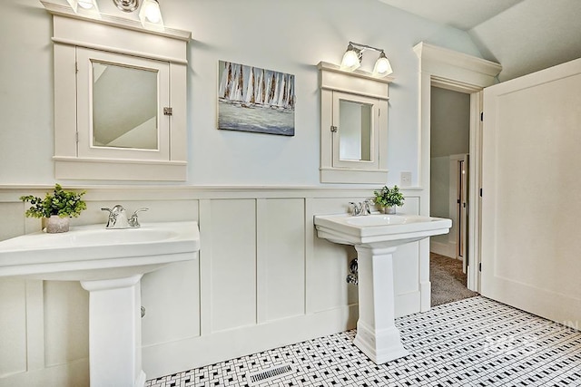 bathroom with a sink, a wainscoted wall, vaulted ceiling, and a decorative wall