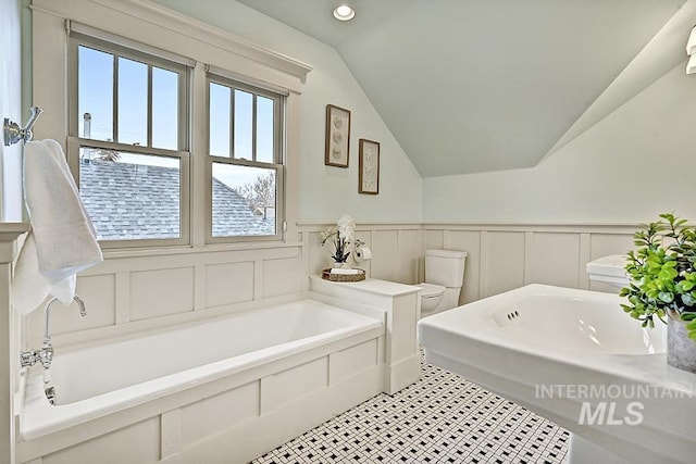 full bath with toilet, lofted ceiling, a garden tub, recessed lighting, and wainscoting