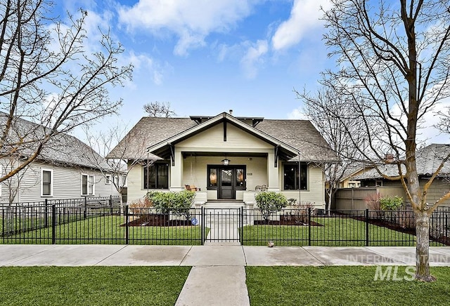 bungalow featuring a fenced front yard, a front lawn, and roof with shingles