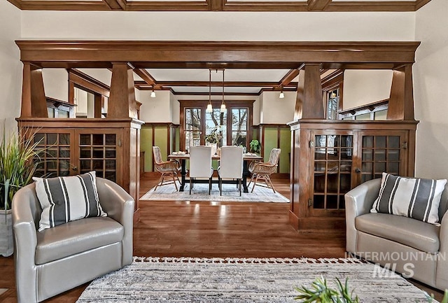 living area with beam ceiling, crown molding, wood finished floors, and a wainscoted wall