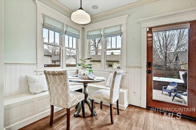 dining space with a wealth of natural light, wood finished floors, wainscoting, and crown molding