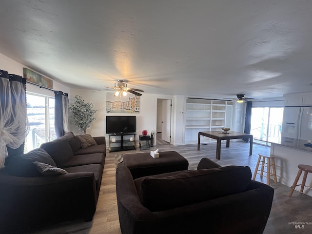 living room with light wood-style flooring, built in shelves, and a ceiling fan