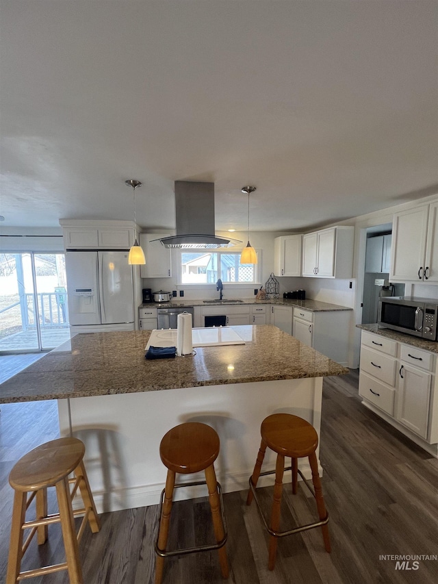 kitchen with island range hood, a kitchen island, white cabinetry, white fridge with ice dispenser, and stainless steel microwave