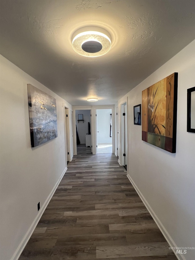 hallway featuring a textured ceiling, dark wood-style flooring, and baseboards