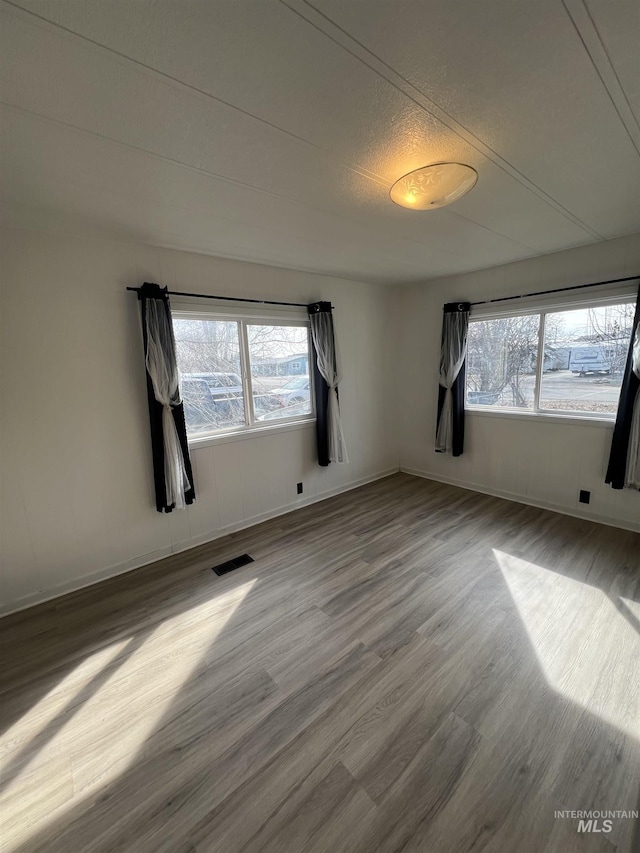 empty room with plenty of natural light, wood finished floors, visible vents, and baseboards