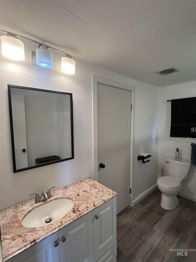 bathroom with visible vents, toilet, vanity, a textured ceiling, and wood finished floors