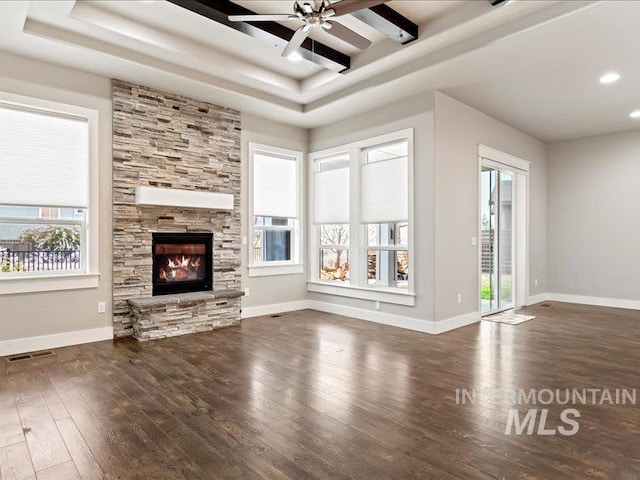 unfurnished living room featuring a fireplace, a healthy amount of sunlight, dark hardwood / wood-style flooring, and a raised ceiling